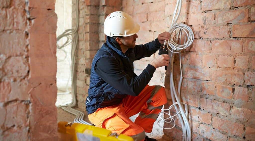 An electrical working on cabling by a brick wall.