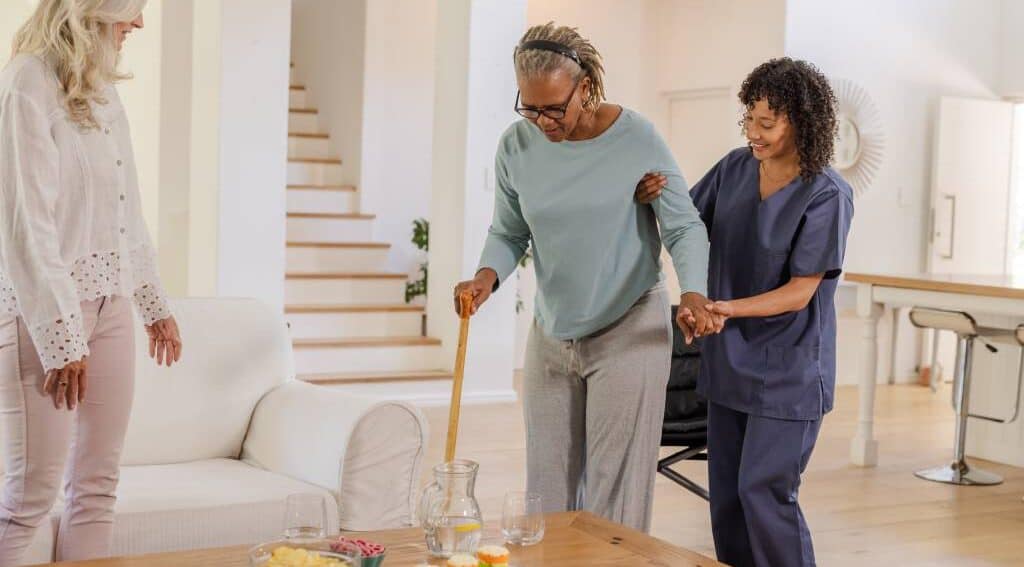 A home healthcare nurse helping a woman walk with a cane.